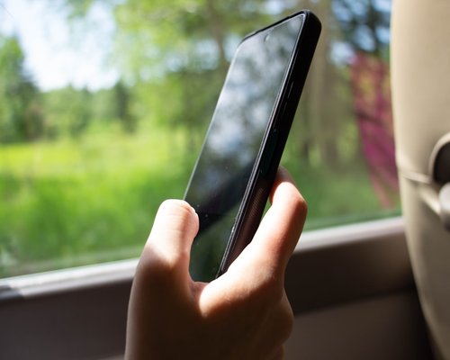 Person holding a smartphone while commuting on a bright sunny day