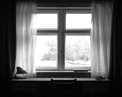 A well lit desk placed next to a window with soft sheer curtains